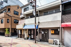 A street view with a row of buildings, including a two-story brick building with a balcony and a ground-level shop with a blue awning. - Midoribashi (Osaka)