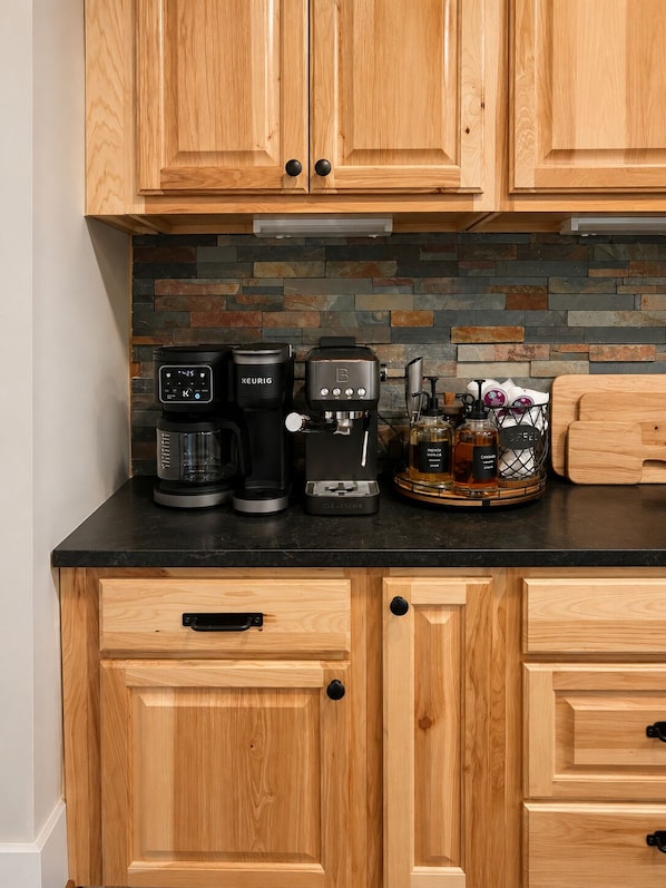 A kitchen with wooden cabinets, a black countertop, and a coffee maker.