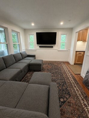 A modern living room with a sectional sofa, a flat-screen TV mounted on the wall, and a patterned rug.