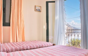 Ein Schlafzimmer mit Bett, Vorhängen, einem gerahmten Bild an der Wand und einem Balkon mit Blick auf einen Berg und Wasser.