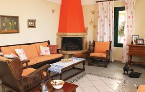 A living room with a fireplace, a sofa, a chair, a table with a bowl of fruit, and a decorative bird. - Cozy home in Loutra Aidipsou with WiFi (Loutra Aidipsou)