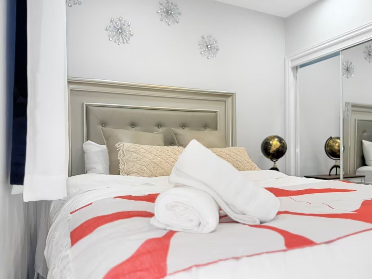 A neatly made bed with a red and white bedspread, a rolled white towel, and a headboard with a tufted design.