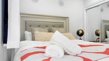 A neatly made bed with a red and white bedspread, a rolled white towel, and a headboard with a tufted design.