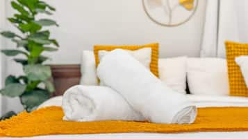 Un lit bien fait, avec du linge de lit blanc et un plaid jaune, une plante sur la gauche et un mur orné d’un motif circulaire.
