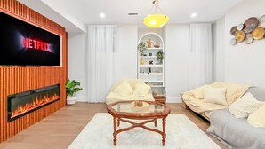 Een woonkamer met een flatscreen televisie, een open haard, een glazen salontafel, een bank en een decoratief wandobject.