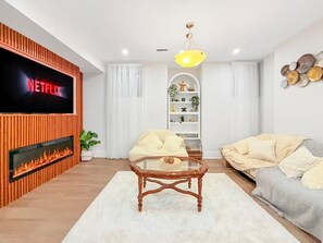 Uma sala de estar com televisão de tela plana, lareira, mesa de centro de vidro, sofá e um objeto decorativo na parede.