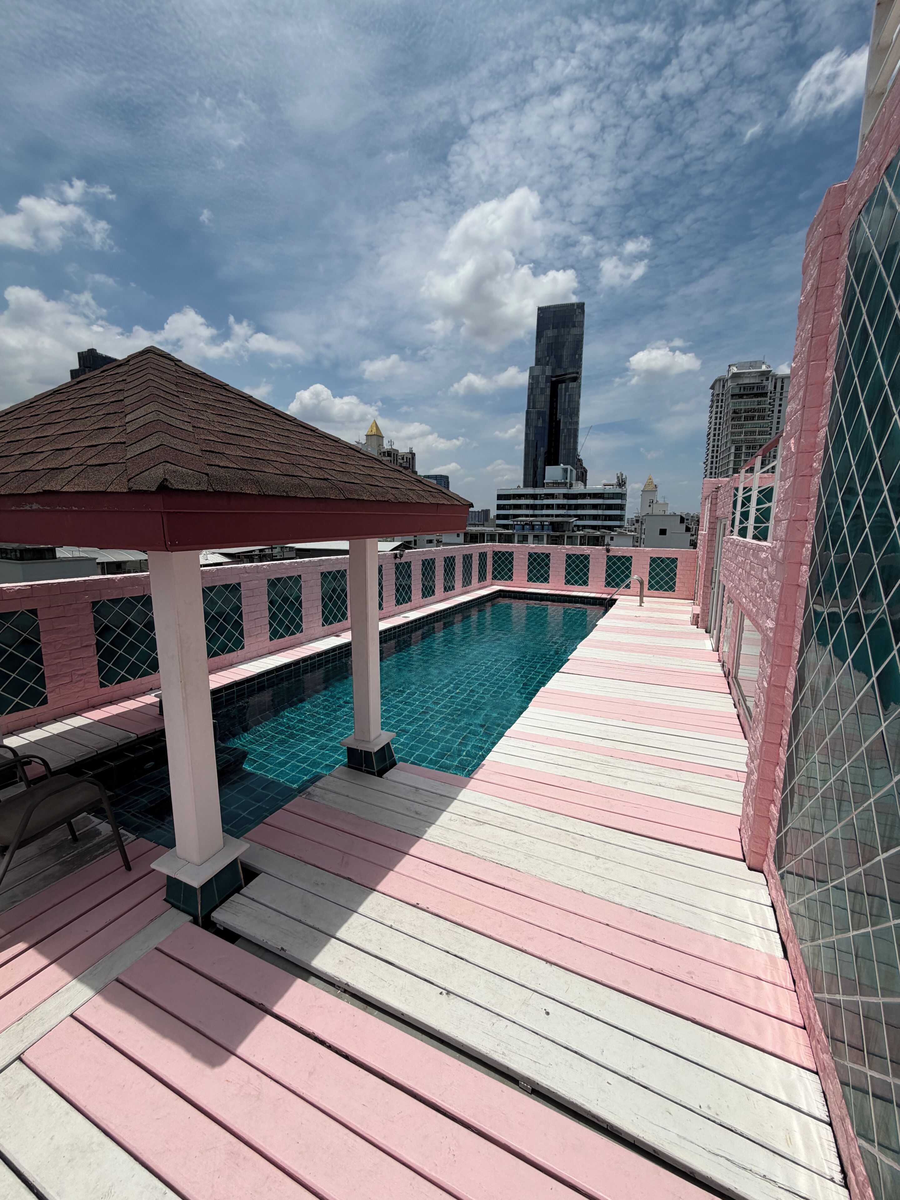 A rooftop pool with a wooden deck, a gazebo, and a view of the city skyline.