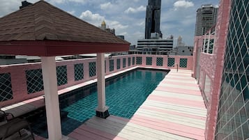 A rooftop pool with a wooden deck, a gazebo, and a view of the city skyline.