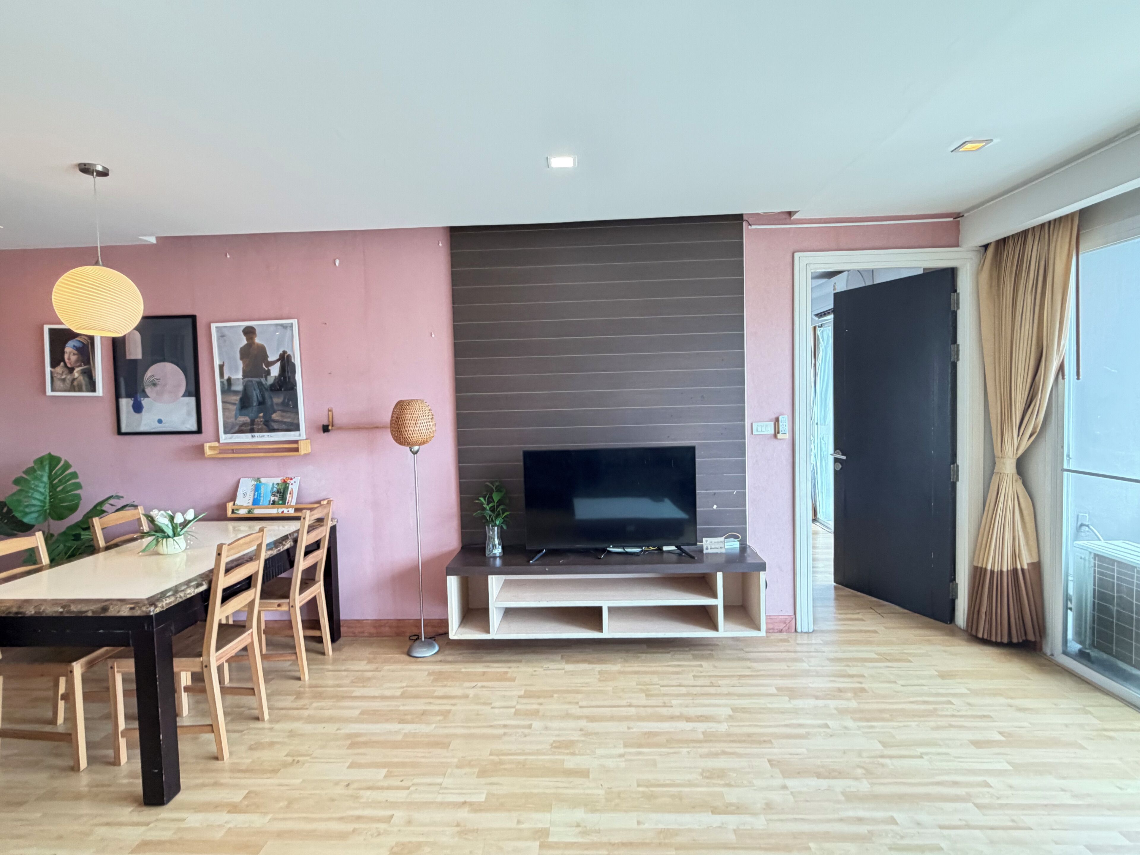 A modern living room with a flat-screen TV, wooden flooring, and a dining area with a table and chairs.