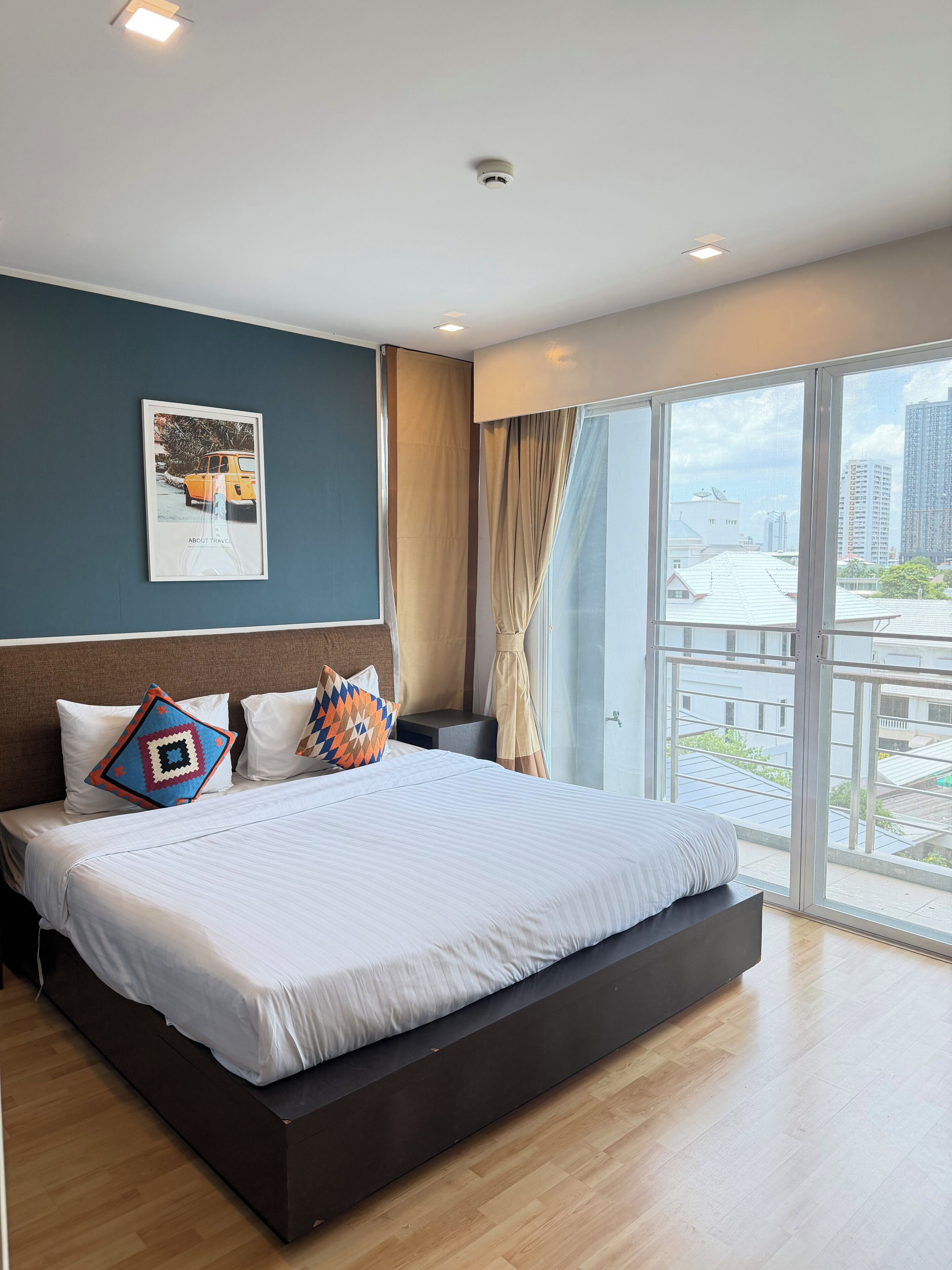 A modern hotel room with a large bed, a city view through the window, and a framed picture on the wall.