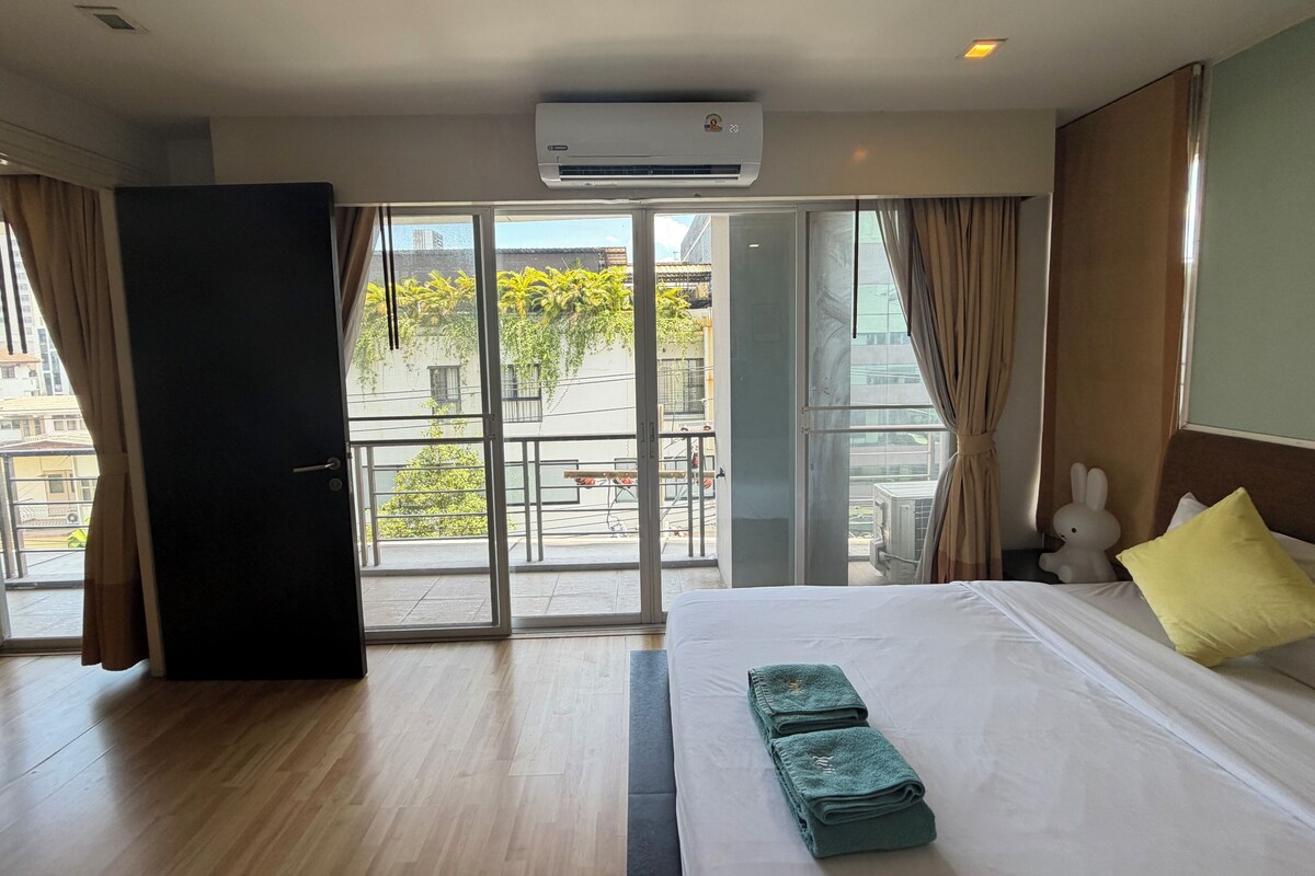 A hotel room with a bed, a window with curtains, an air conditioning unit, and a view of the outside.