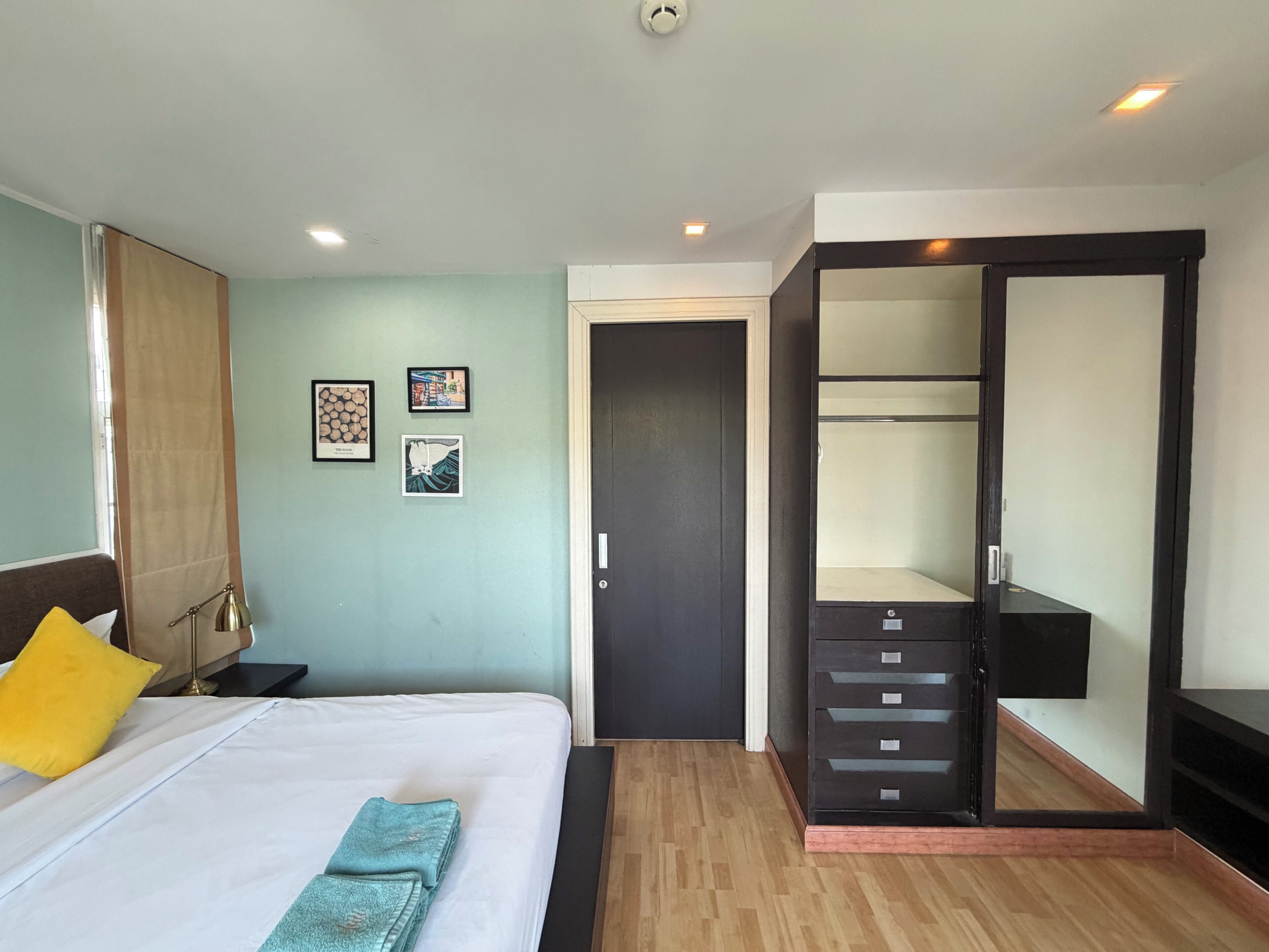 A hotel room with a bed, bedside table, lamp, and a wardrobe with a mirror.