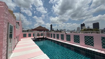 A rooftop pool with a pink and white deck, surrounded by a city skyline.