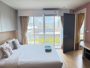 A hotel room with a bed, curtains, an air conditioning unit, a view of buildings and greenery, and a door. - P Residence Thonglor  (Bangkok)