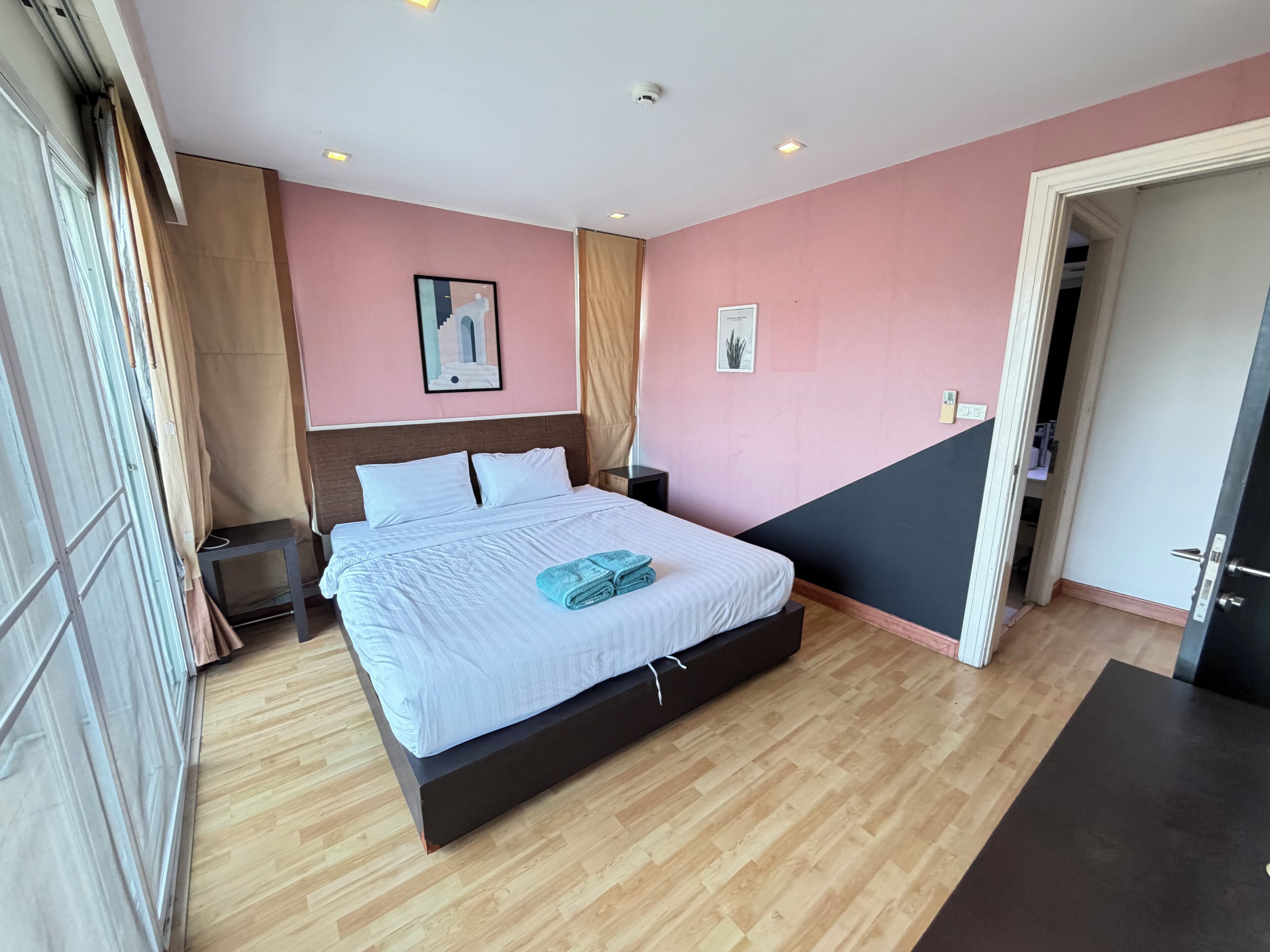 Un dormitorio moderno con una cama grande, una mesita de noche, un estante en la pared y una puerta que da a otra habitación.