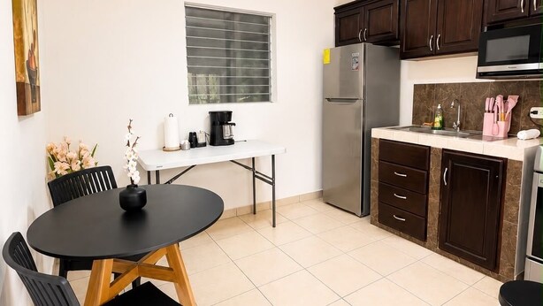 A compact kitchen with a dining area, equipped with a refrigerator, microwave, and a coffee maker.