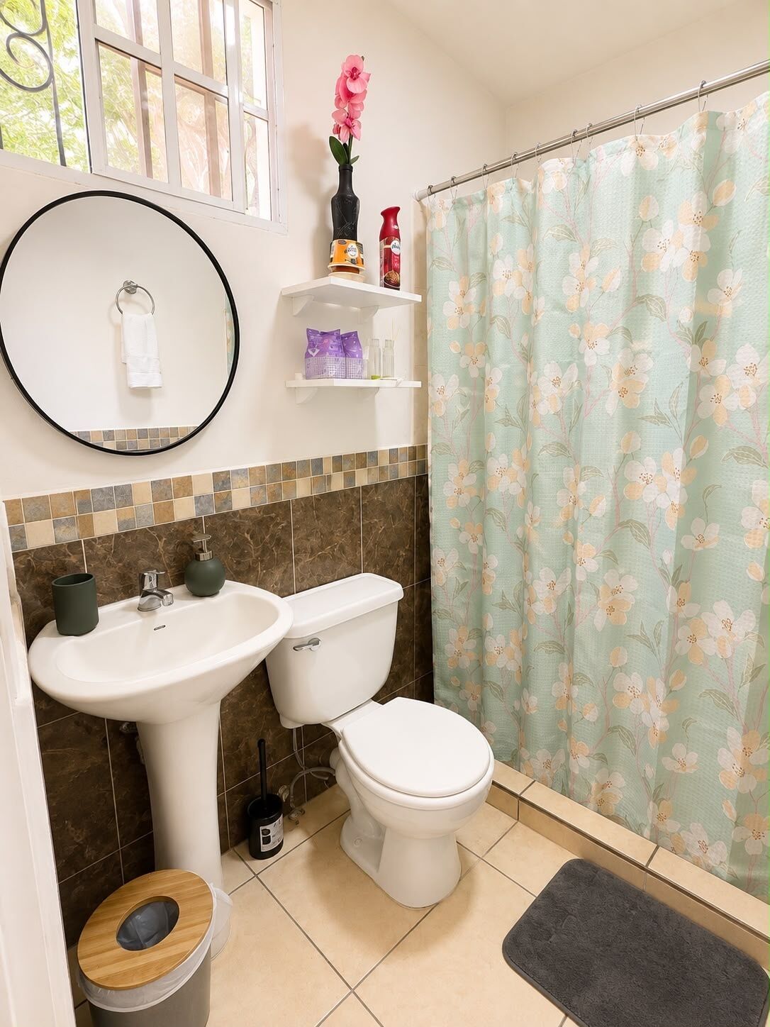 Une salle de bain équipée de toilettes, d’un lavabo et d’un rideau de douche à motifs floraux.