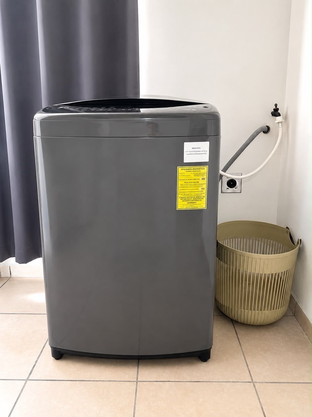 A compact, grey appliance, possibly a vacuum cleaner, with a label indicating energy efficiency. It is placed on a tiled floor next to a beige basket and a power outlet.