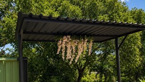 An outdoor bar area with a pergola, three wooden bar stools, and hanging flowers.