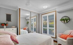 A bedroom with a bed, a dresser, a mirror, a window with blinds, and a potted plant. - Summit House - Elevated Family Retreat (Mackay)