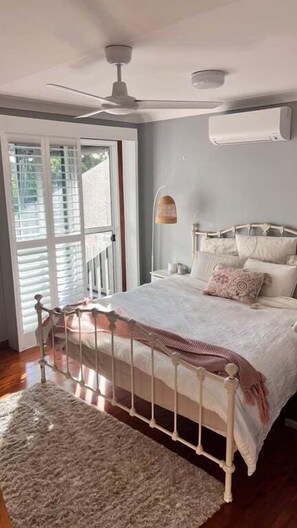 A bedroom with a bed, a ceiling fan, an air conditioning unit, and a view through a sliding glass door.