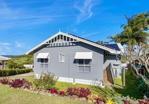 A single-story house with a gabled roof, a front porch, and a small garden with various plants. - Summit House - Elevated Family Retreat (Mackay)