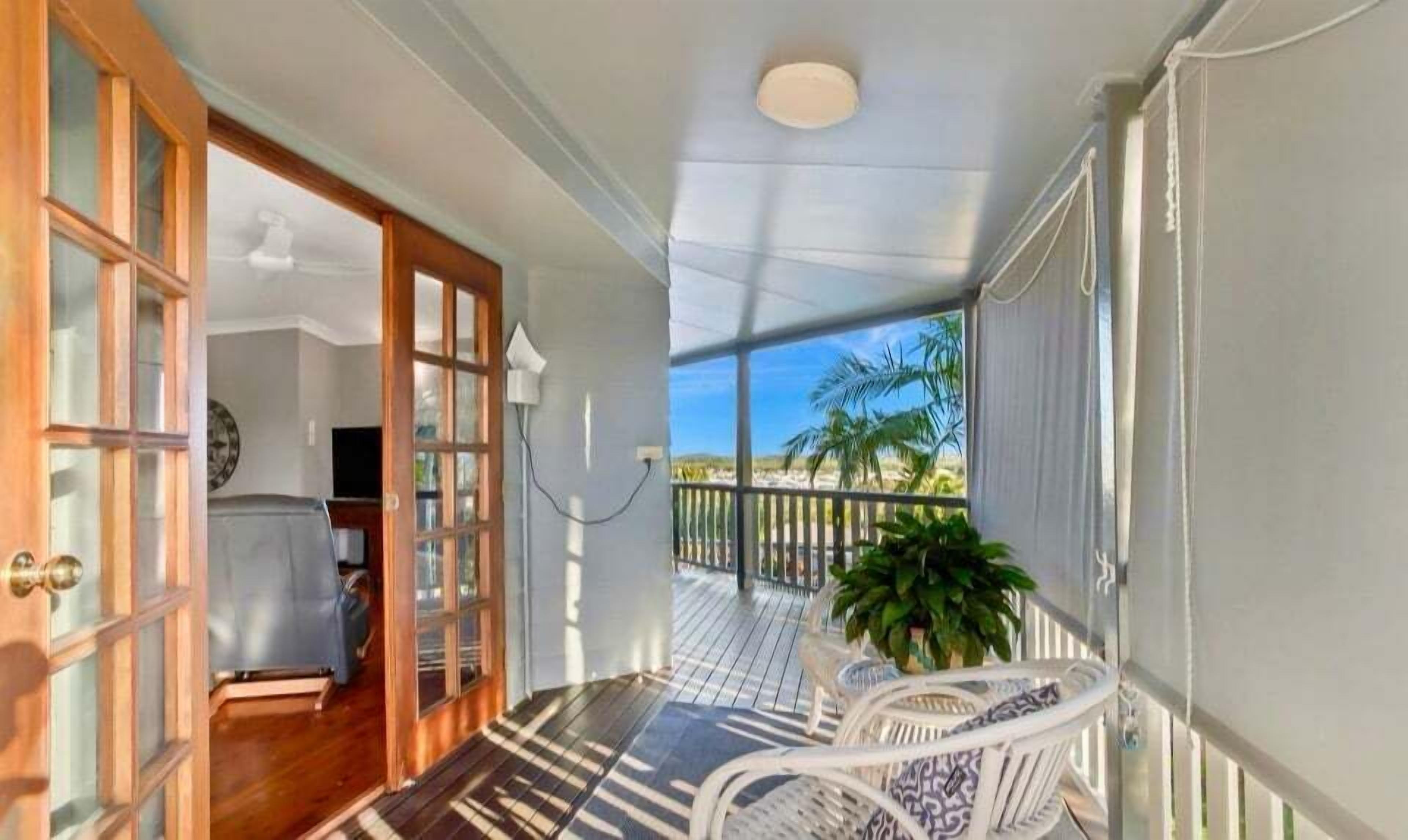 A covered porch with a view of the landscape, a door leading to a room, and a potted plant.