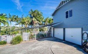 Ein Wohnhaus mit Garage, überdachter Auffahrt und einem durch Zäune gesicherten Garten mit Palmen.