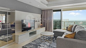 A modern living room with a flat-screen TV, a sofa, a coffee table, and a large window offering a city view. - Cavren by Kozystay - MERR (Surabaya)