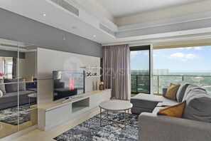 A modern living room with a flat-screen TV, a sofa, a coffee table, and a large window offering a city view. - Cavren by Kozystay - MERR (Surabaya)