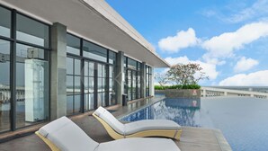 A rooftop infinity pool with two lounge chairs, a clear sky, and a view of the cityscape. - Cavren by Kozystay - MERR (Surabaya)
