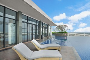 A rooftop infinity pool with two lounge chairs, a clear sky, and a view of the cityscape. - Cavren by Kozystay - MERR (Surabaya)
