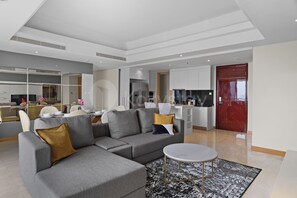 A modern living room with a sectional sofa, a round coffee table, and a dining area with chairs and a table. - Cavren by Kozystay - MERR (Surabaya)