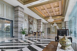 A spacious lobby with a marble floor, a chandelier, and a seating area with a table and chairs. - Cavren by Kozystay - MERR (Surabaya)