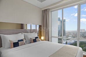 A hotel room with a large bed, a nightstand, and a view of a cityscape through a large window. - Cavren by Kozystay - MERR (Surabaya)