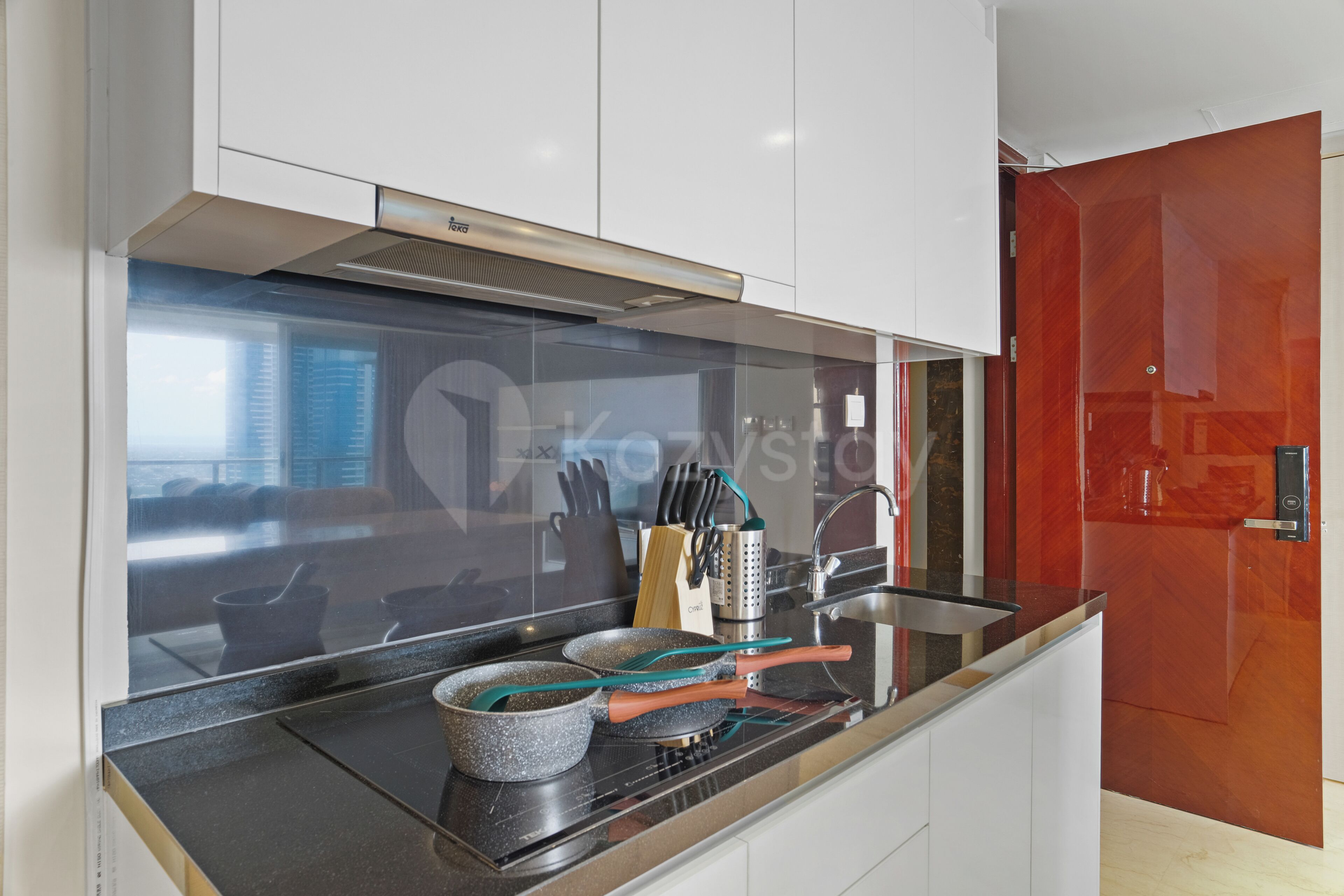 A modern kitchen with a black countertop, stainless steel appliances, and a red door.