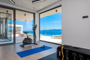 A modern gym with exercise equipment, a blue mat, and a view of the sea through large windows. - Villa rOvni, Labin, Croatia (Labin)