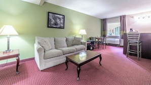 Habitación de hotel con pared verde, sofá, mesa de centro, escritorio, silla, lámpara e imagen en un marco.