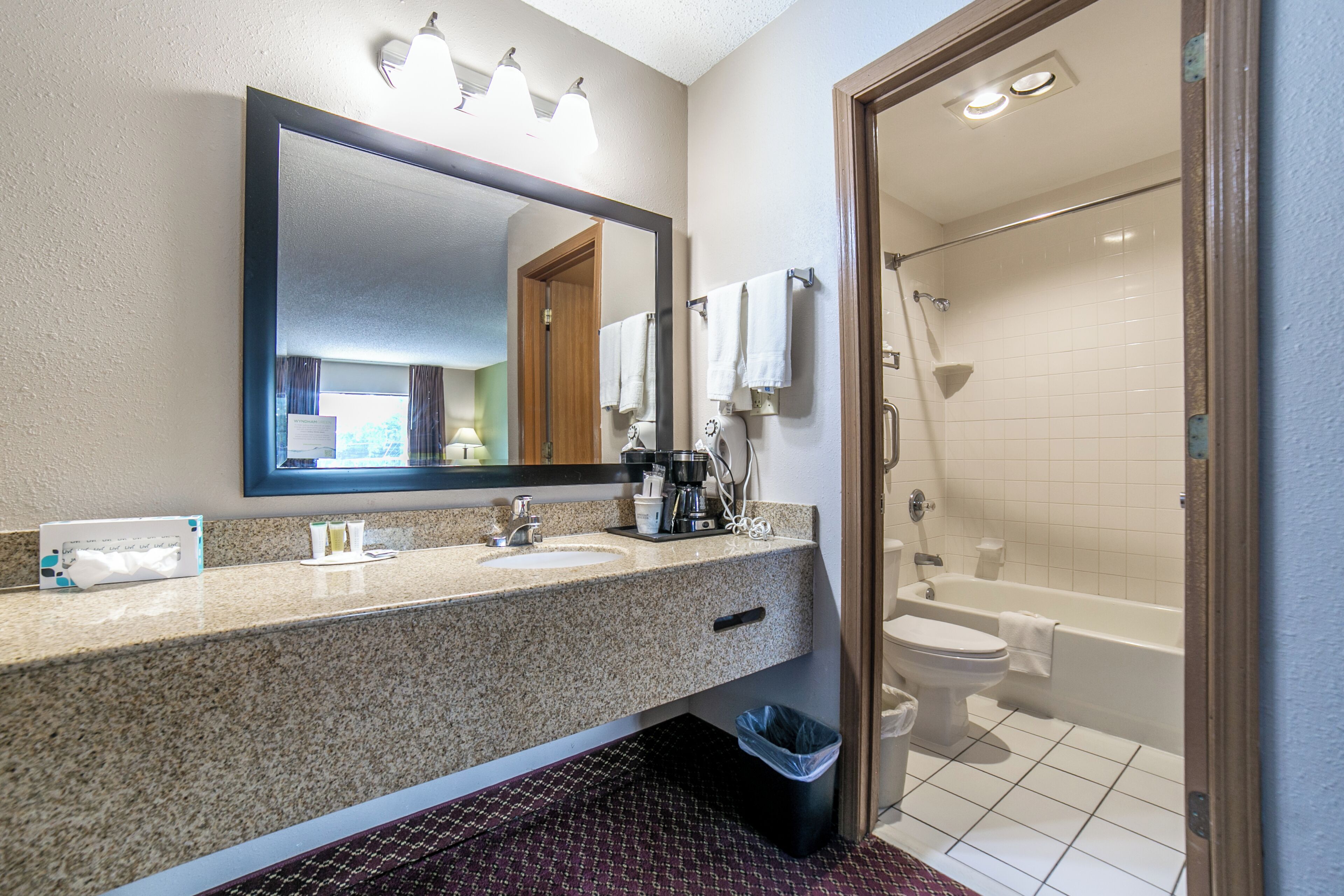 Un baño de hotel con lavamanos, espejo, toallero y zona de ducha.