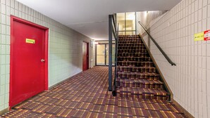 Un pasillo con una puerta roja, alfombra estampada y una escalera con barandilla de metal.