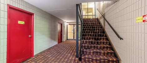 Un pasillo con una puerta roja, alfombra estampada y una escalera con barandilla de metal.
