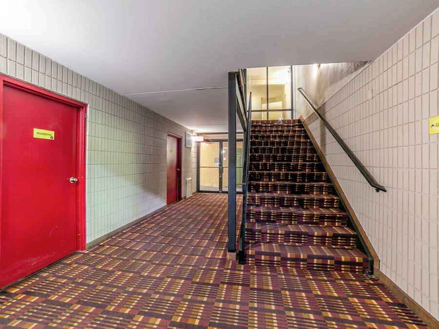 Un pasillo con una puerta roja, alfombra estampada y una escalera con barandilla de metal.