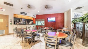 Un restaurante con varias mesas y sillas, una estación de café y una pantalla de televisión que muestra un menú.
