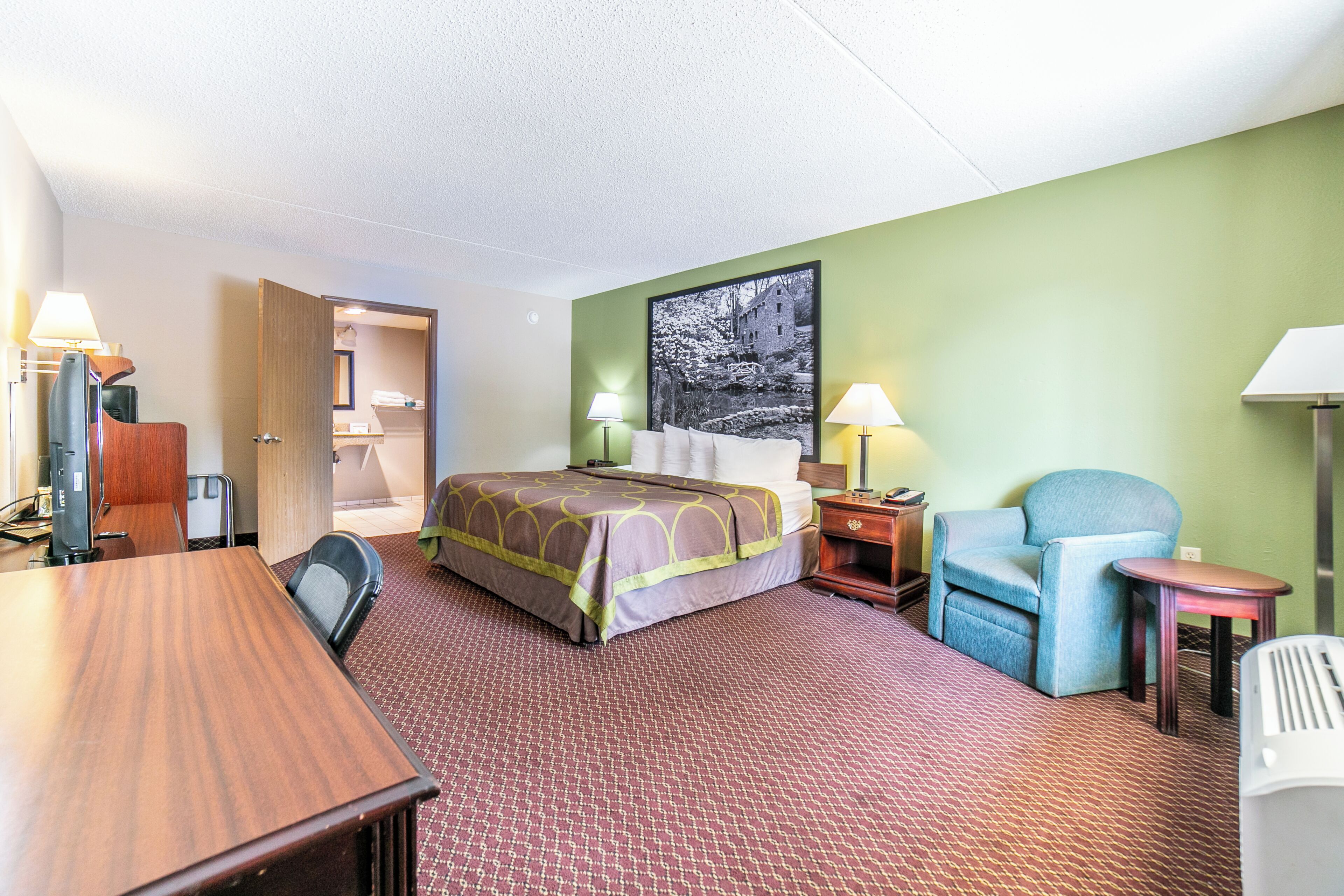 Une chambre d’hôtel équipée d’un lit, d’un bureau, d’une chaise, d’une petite table et d’un téléviseur fixé au mur.