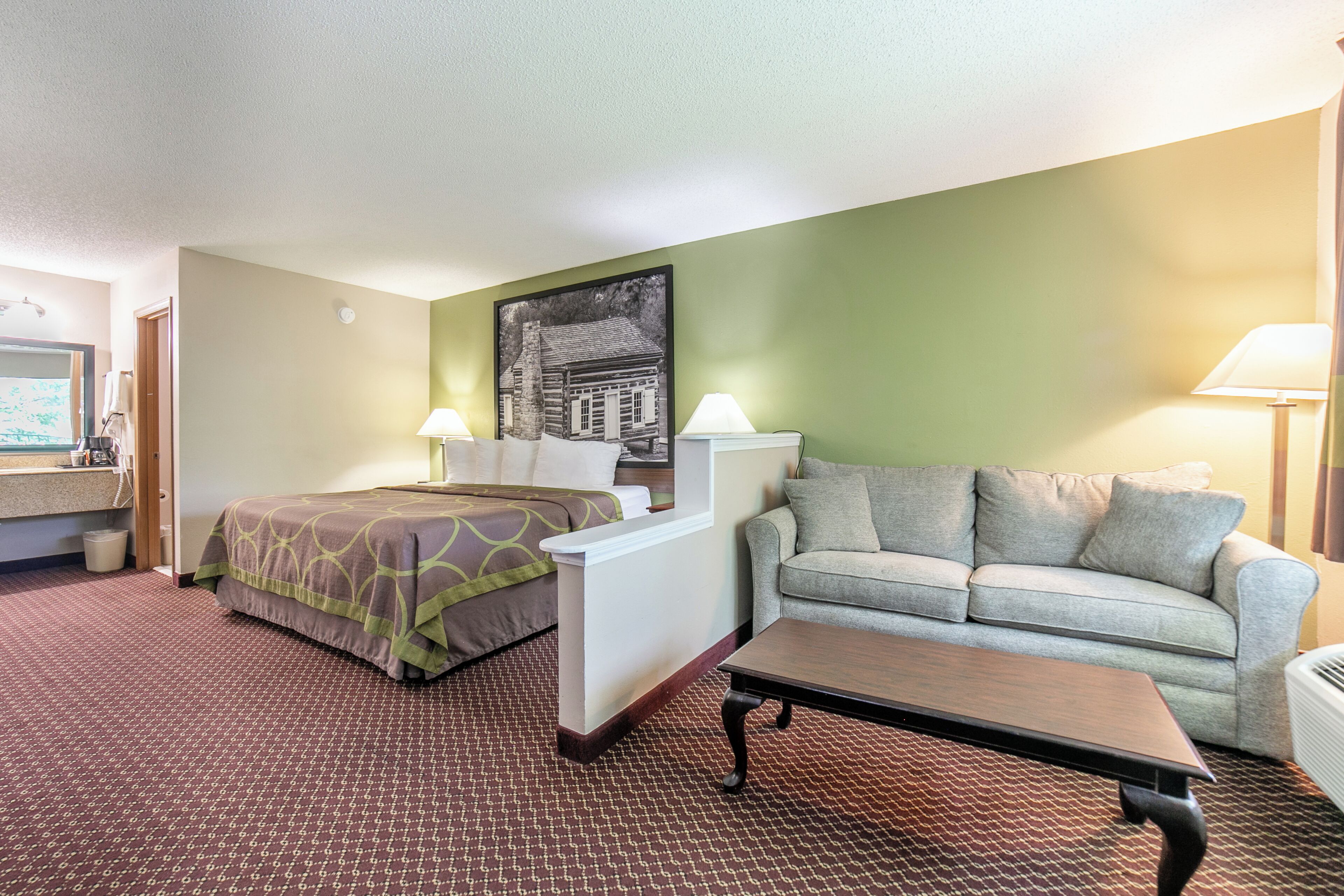 A hotel room with a bed, a sofa, a table, and a painting on the wall.