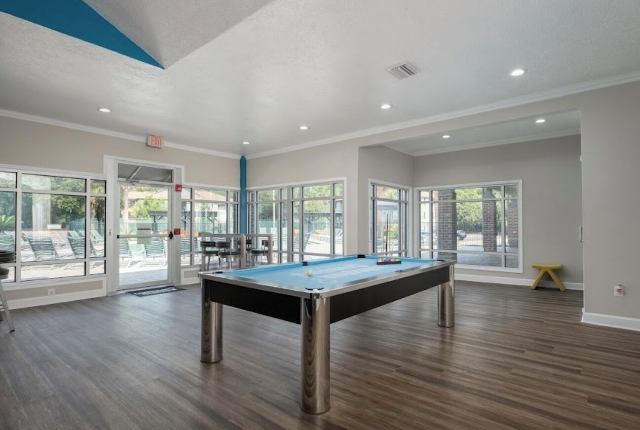 A pool table in a room with large windows, wooden flooring, and a door leading outside.