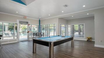 A pool table in a room with large windows, wooden flooring, and a door leading outside.