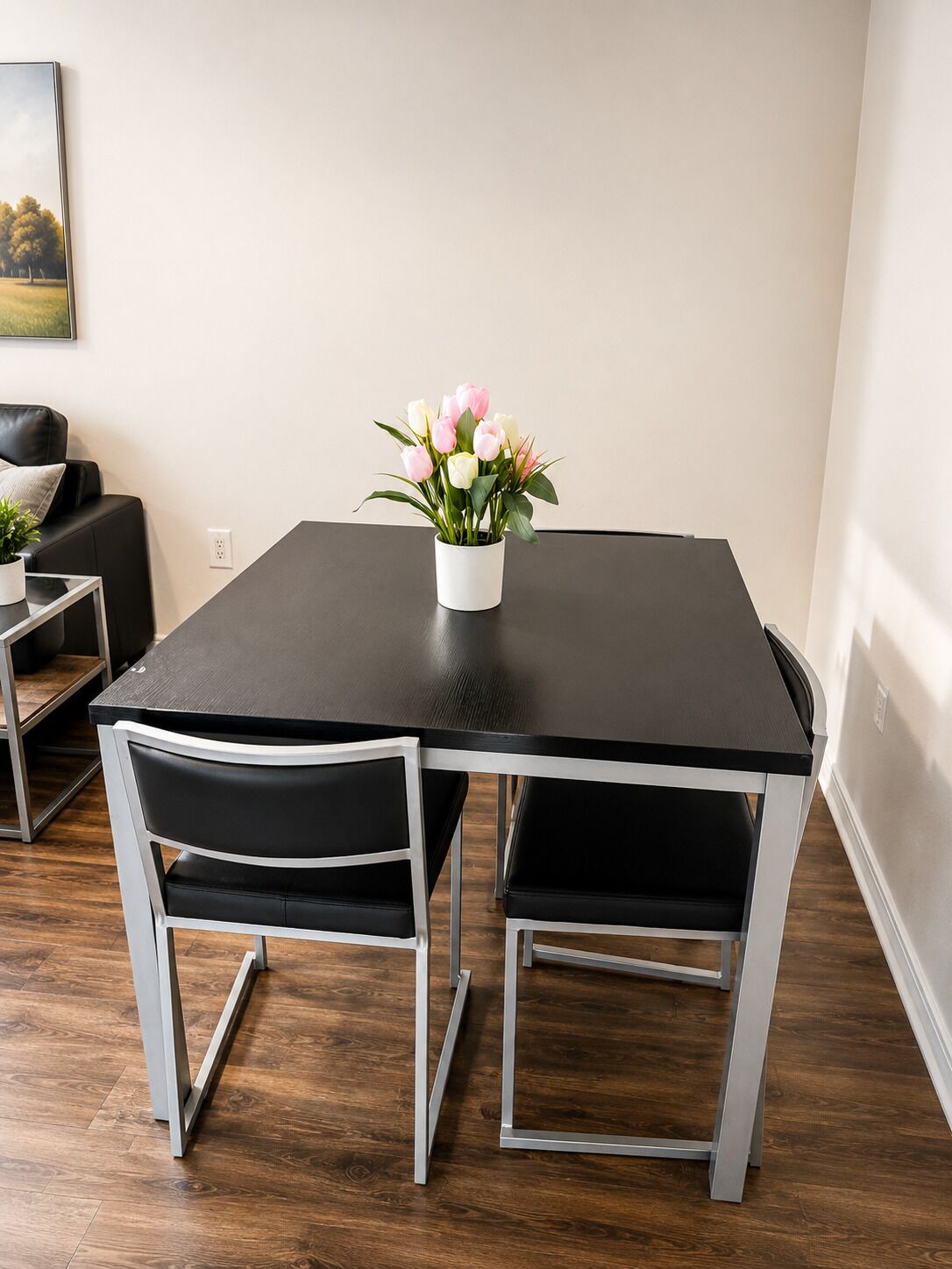 A dining area with a black table, two chairs, and a white vase with flowers.