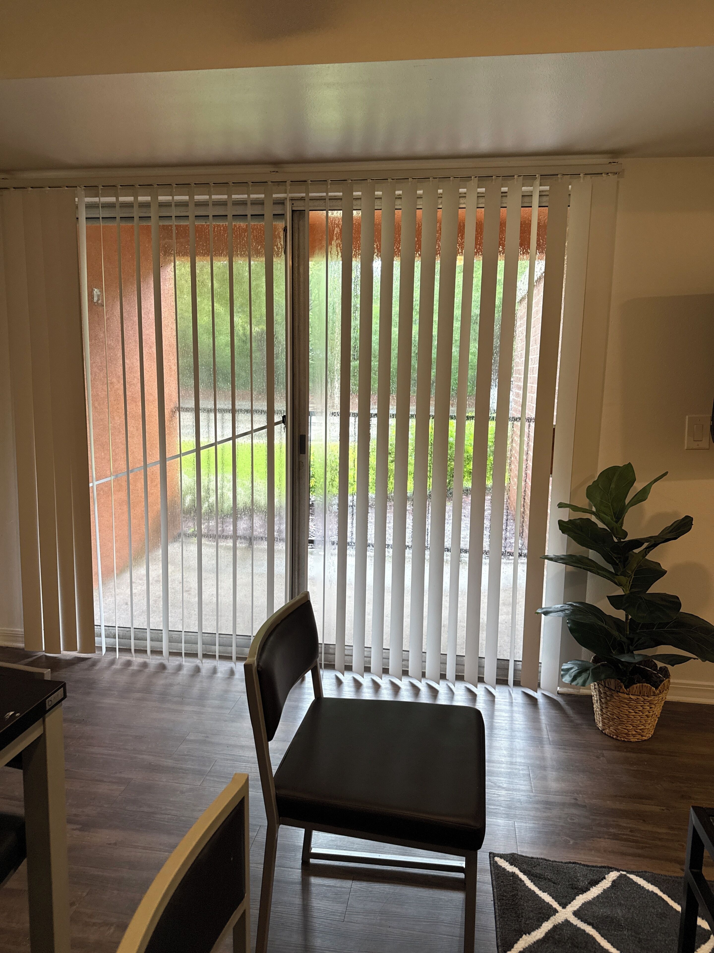 A room with a sliding glass door leading to a patio, a dark leather chair, a woven basket plant, and a black and white rug.