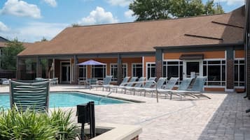 A pool area with lounge chairs and a brick building in the background.